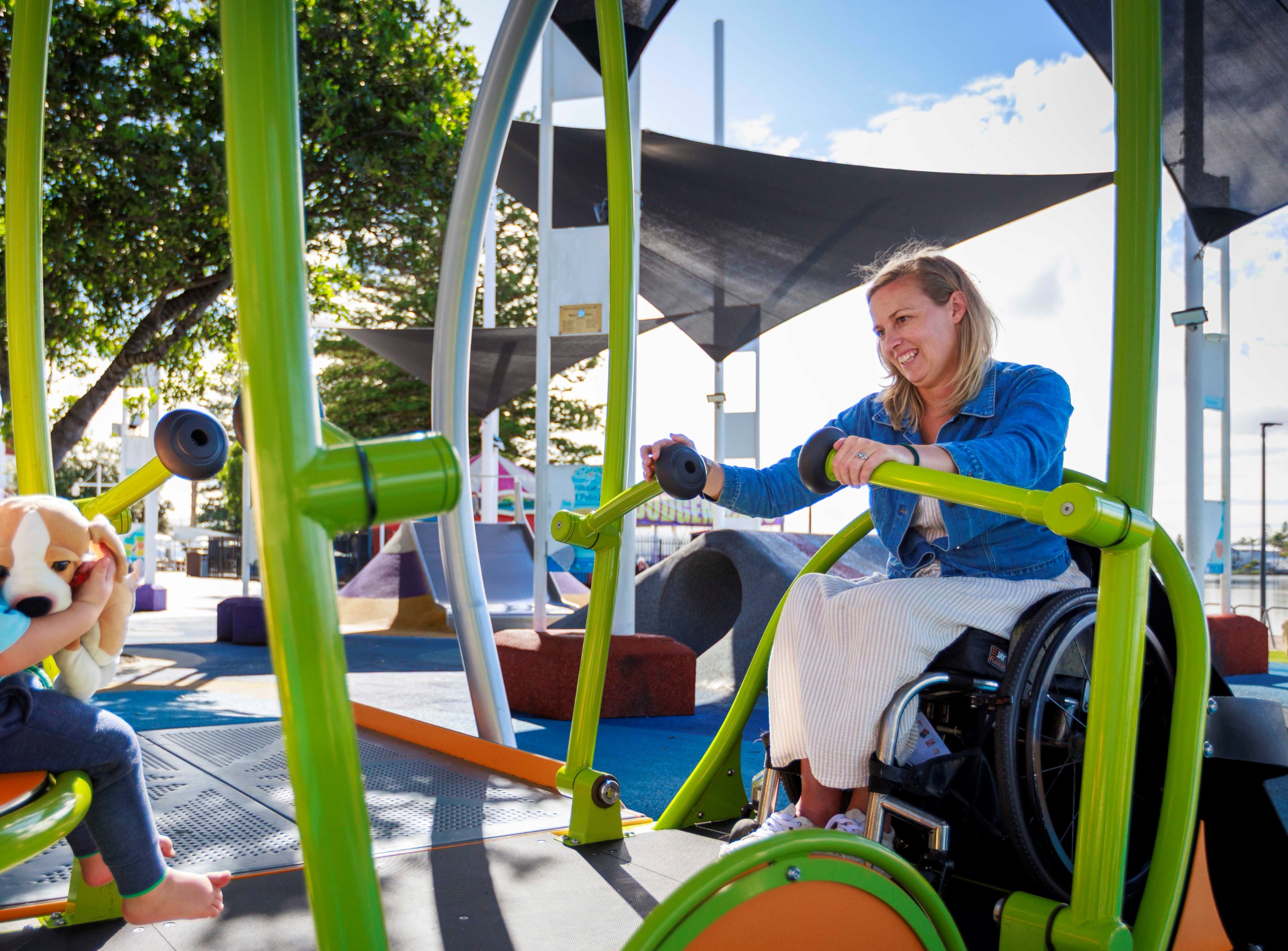A woman in a wheelchair joyfully interacts with a child on a colorful playground