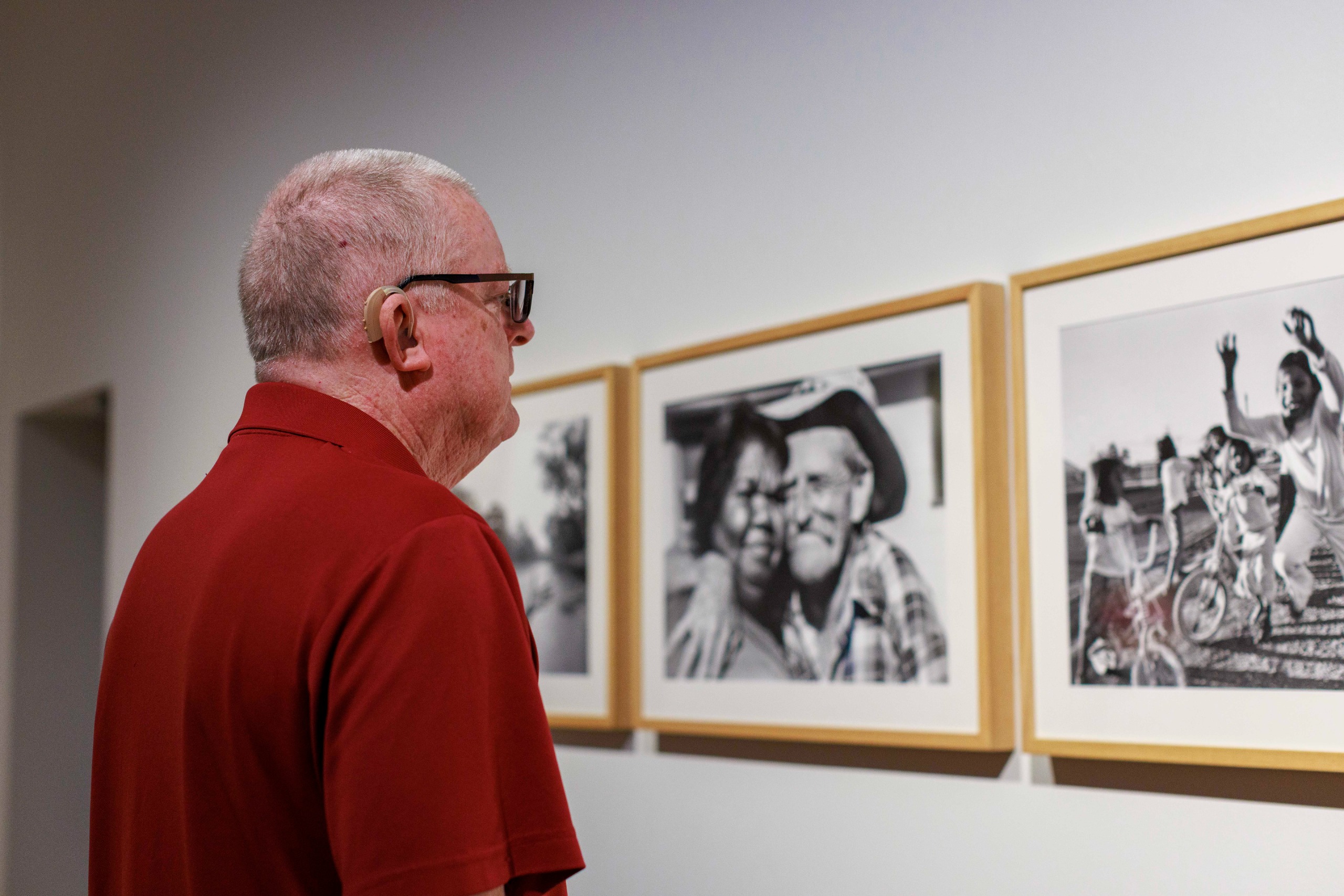 A man with a hearing aid examines photographs displayed in an art gallery