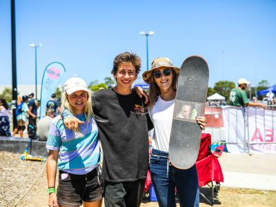 three people smiling at the camera holding skateboards 